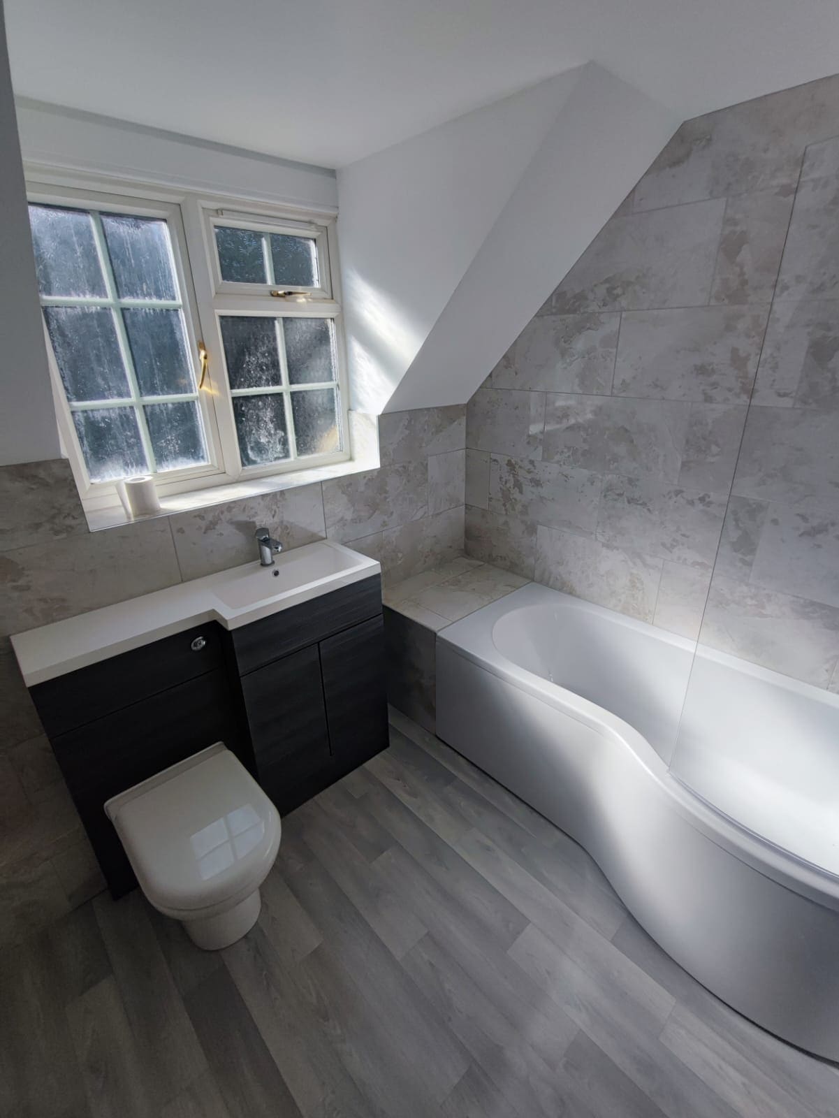 Grey tiled bathroom with P-shaped shower bath and dark vanity unit