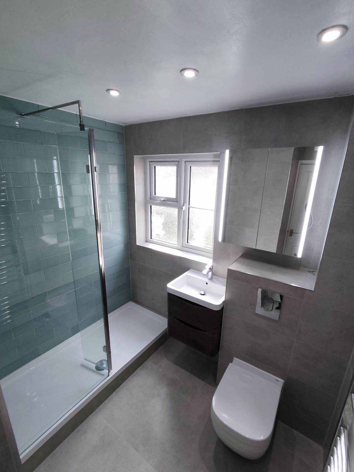 Walk-in shower wet room with green metro tiles and wall-hung toilet